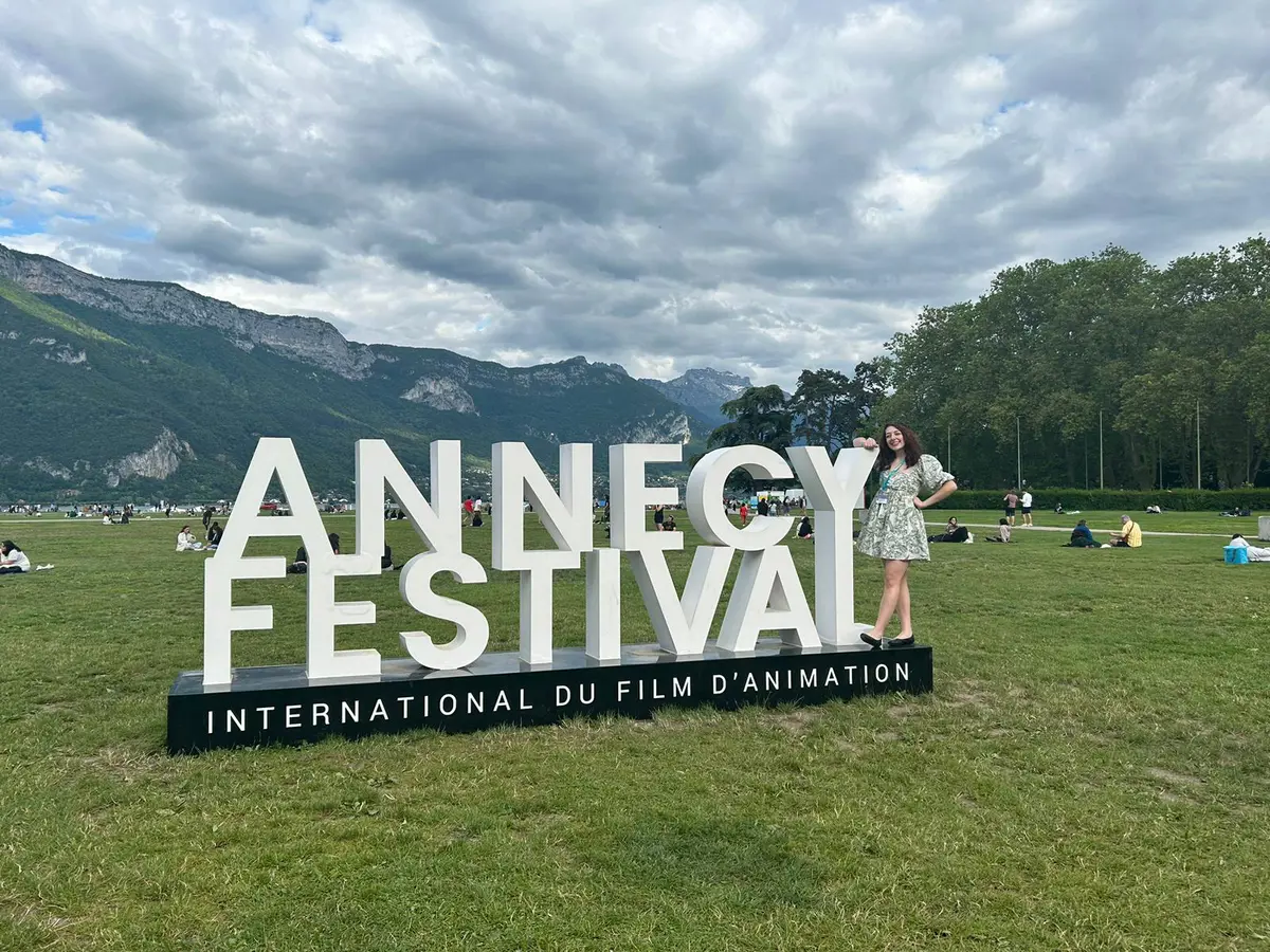 Student standing with Annecy International Animation Film Festival sign with mountains in the background.