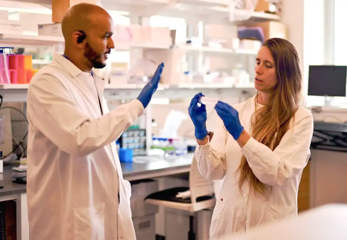 Anyelo Diaz and Chiara Ghezzi work in a lab wearing lab coats and gloves