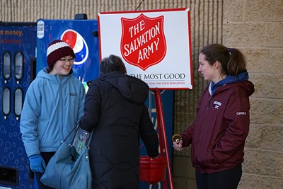 A woman makes a donation in a Salvation Army kettle while volunteer bell ringers look on