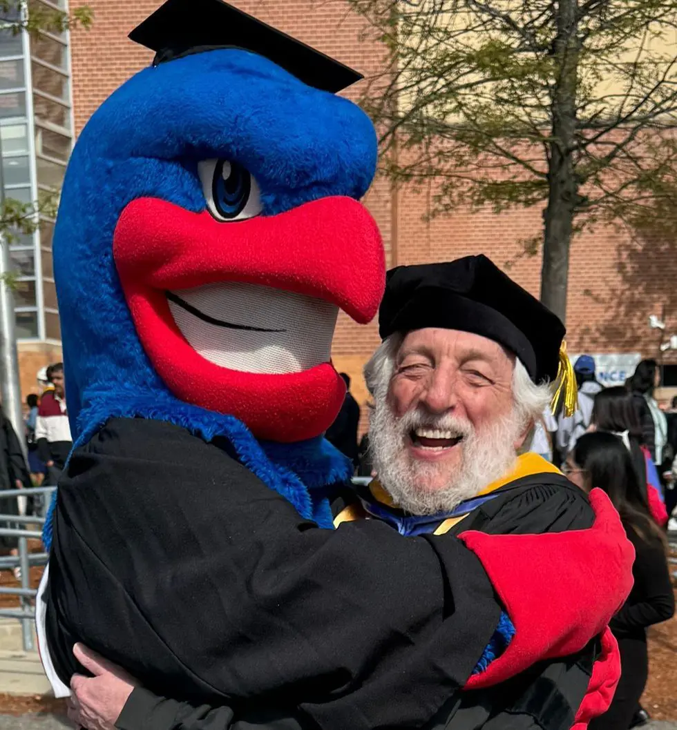 Graduation-garbed Art Mittler gets a hug from Rowdy River Hawk at Commencement