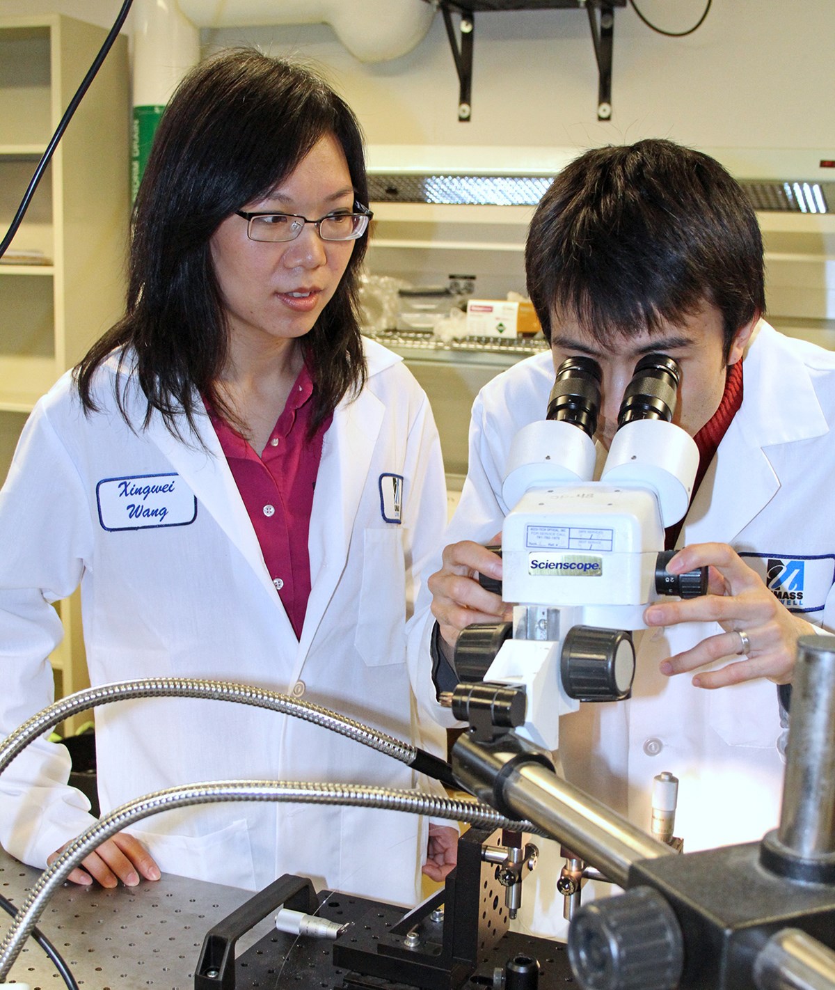 Assoc. Prof Xingwei Wang oversees a male looking into a microscope.