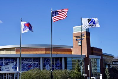 The UMass Lowell and American flags fly in the wind in front of the Tsongas Center