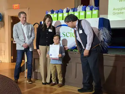 Andover first-grader Auggie Mulligan, holding a certificate, is congratulated by leaders of the Cool Science contest.