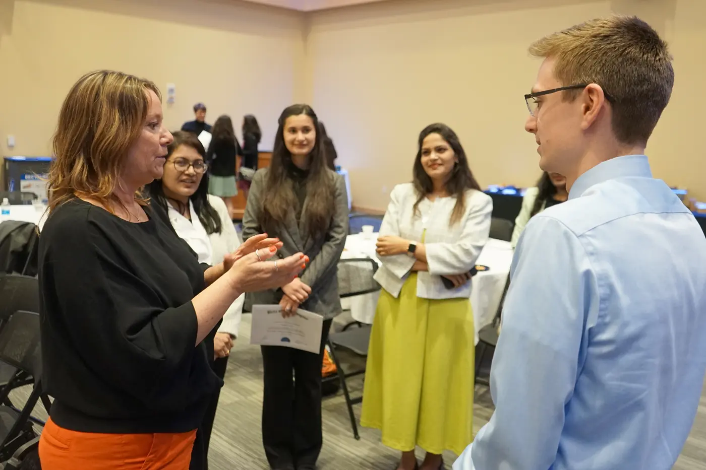 Five people talk in a circle while standing in a large room.