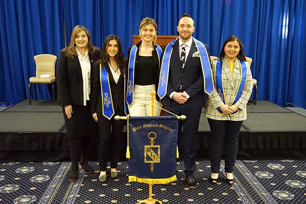 Four women and a man pose for a photo at an honor society induction ceremony