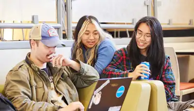 Three students view a laptop together