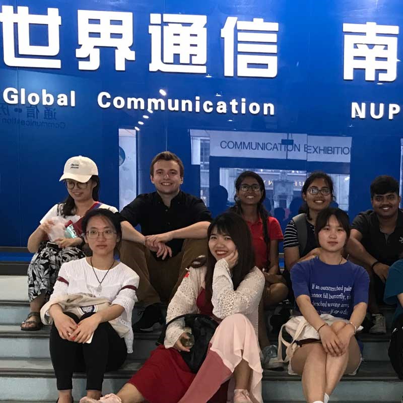 Group of students sit in front of a global communications exhibition sign