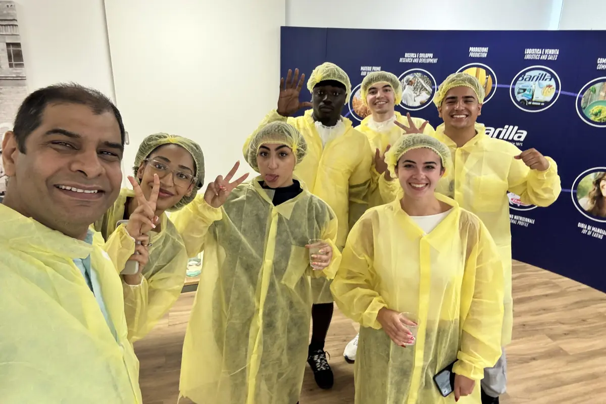Seven people wearing yellow protective gear pose for a photo in a pasta factory.