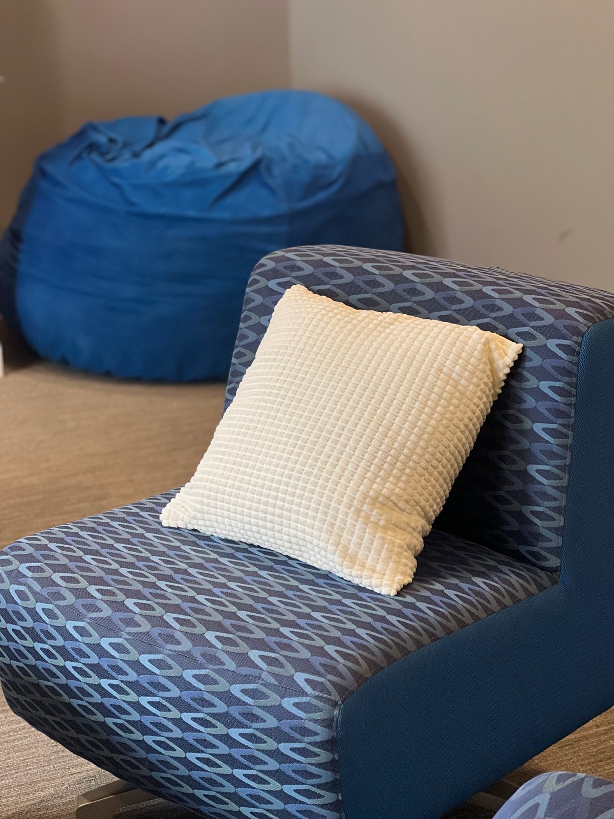 Textured white pillow sitting on patterned lounge chair with a blue bean bag in the background