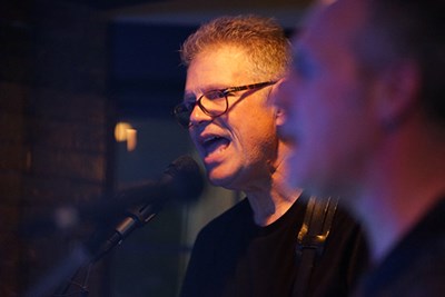 A man in glasses with short hair sings into a microphone