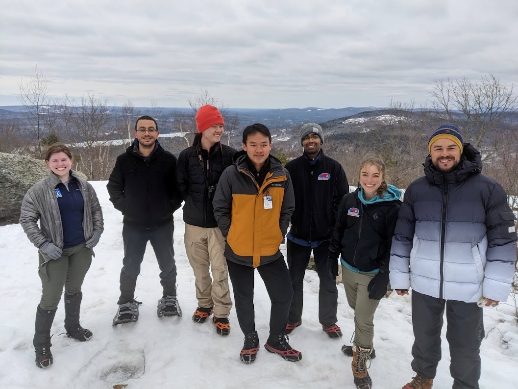 a group of people smiles while they stand atop a snowy overlook