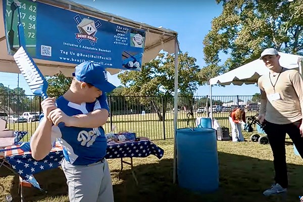 A youngster in a blue baseball uniform sings a blue bat while a young man looks on