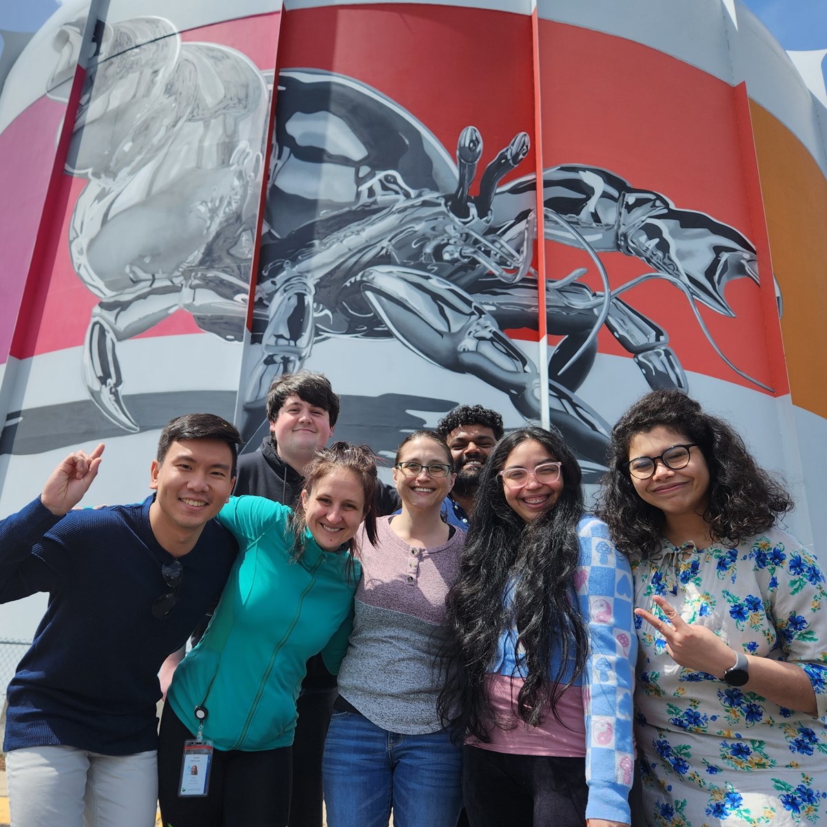Nuclear Forensics students in a group, in front of the reactor containment building.  The building has an artistic rendition of a hermit crab with rainbow colors all around the perimeter