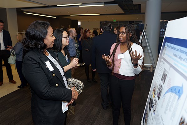 A young woman in glasses explains a poster to two other women at an event