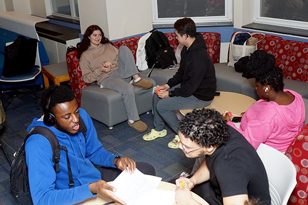 Five college students study and chat in a residence hall lounge.