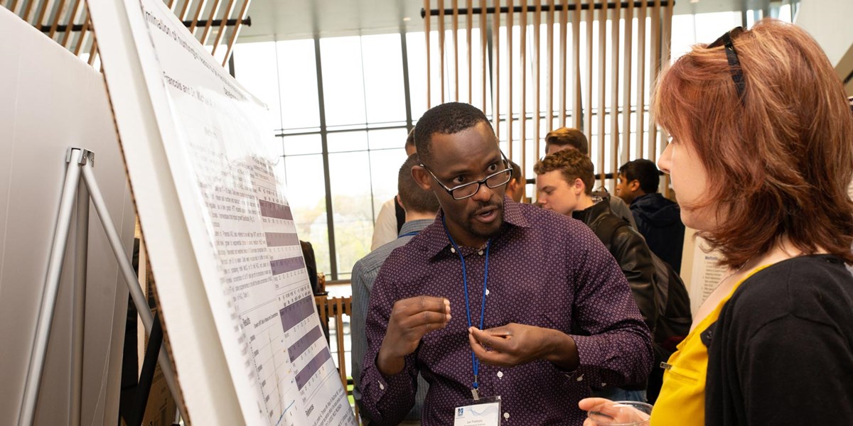 Black man explaining research to woman at 2019 student research symposium