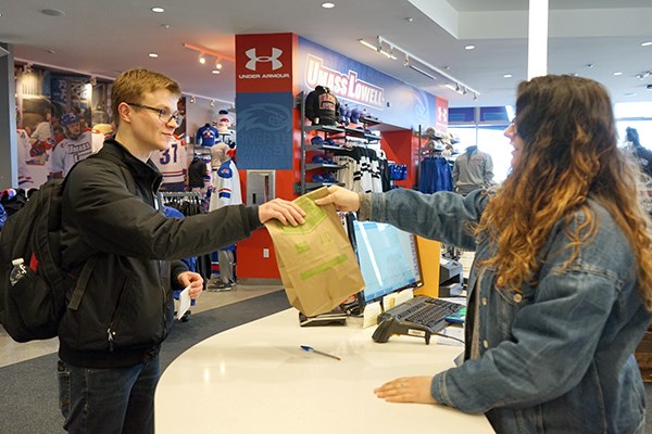Cashier Danielle DePalma hands a student a paper bag at the bookstore