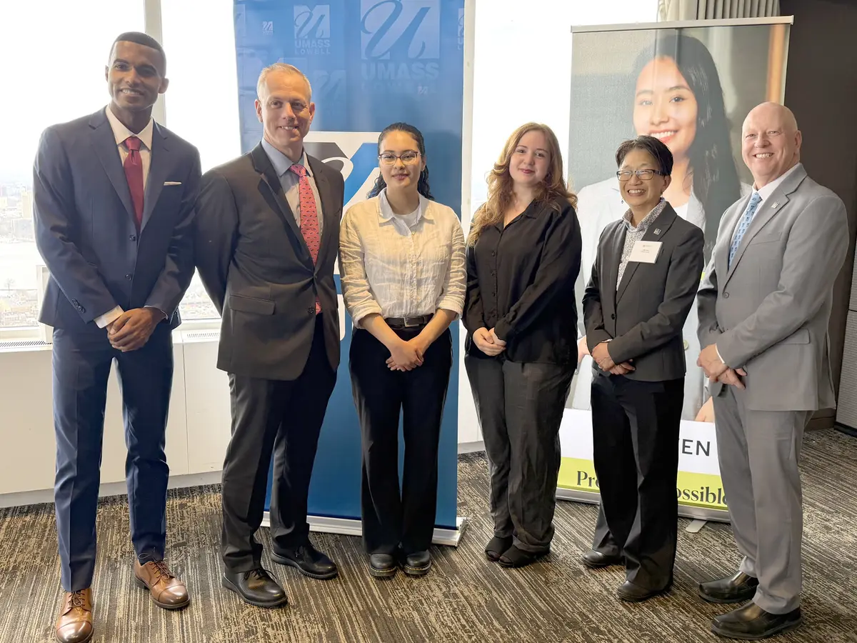 Six people pose for a group photo while standing in front of a window in a room.