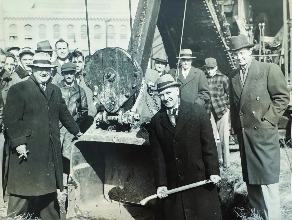 Black and white photo of men in fedoras and top coats at groundbreaking