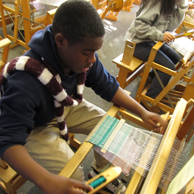 An older boy weaving at a loom at theTsongas Industrial History Center