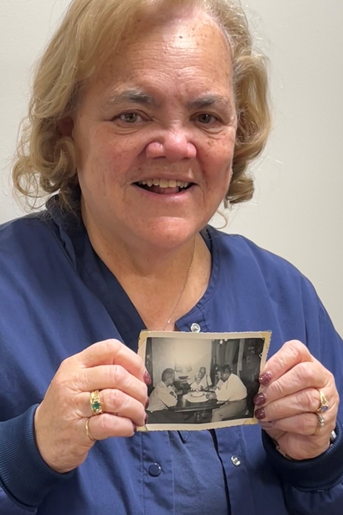 A woman smiles for a picture while holding an old black and white photograph