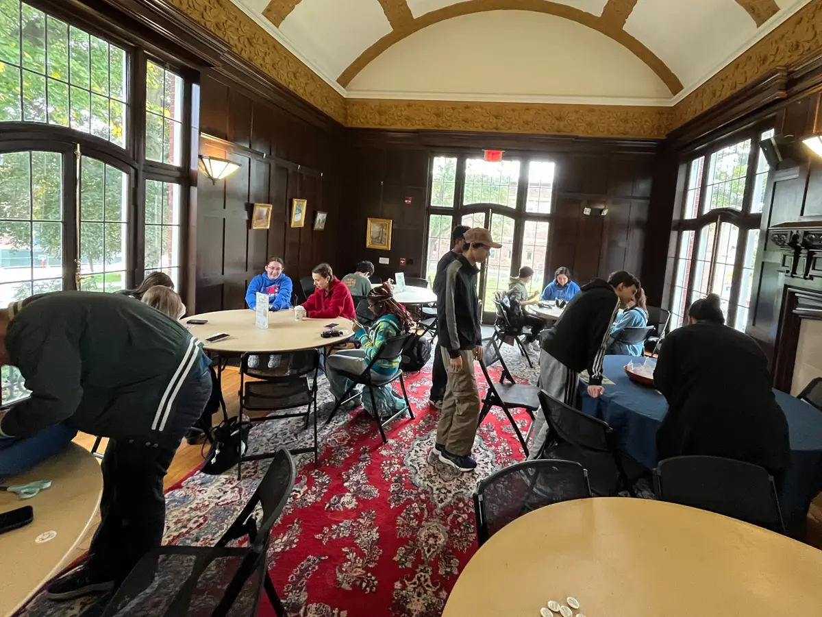 Students sit and stand around tables at button-making event.