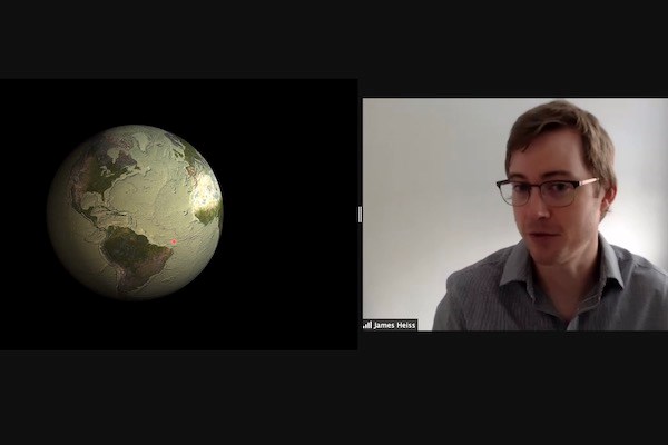 A man in glasses talks on the right side of a videoconference screen. There is a graphic of earth on the left side of the screen.