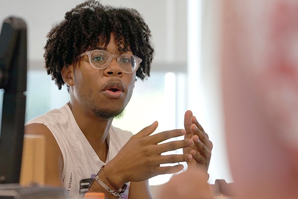 A student with glasses gestures with his hands while talking