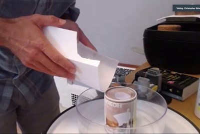 A man holds a piece of paper over a bowl that has a can in the middle