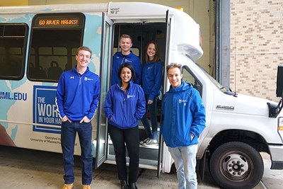 Student trainers and manager Karina Cruz stand in front of a shuttle bus