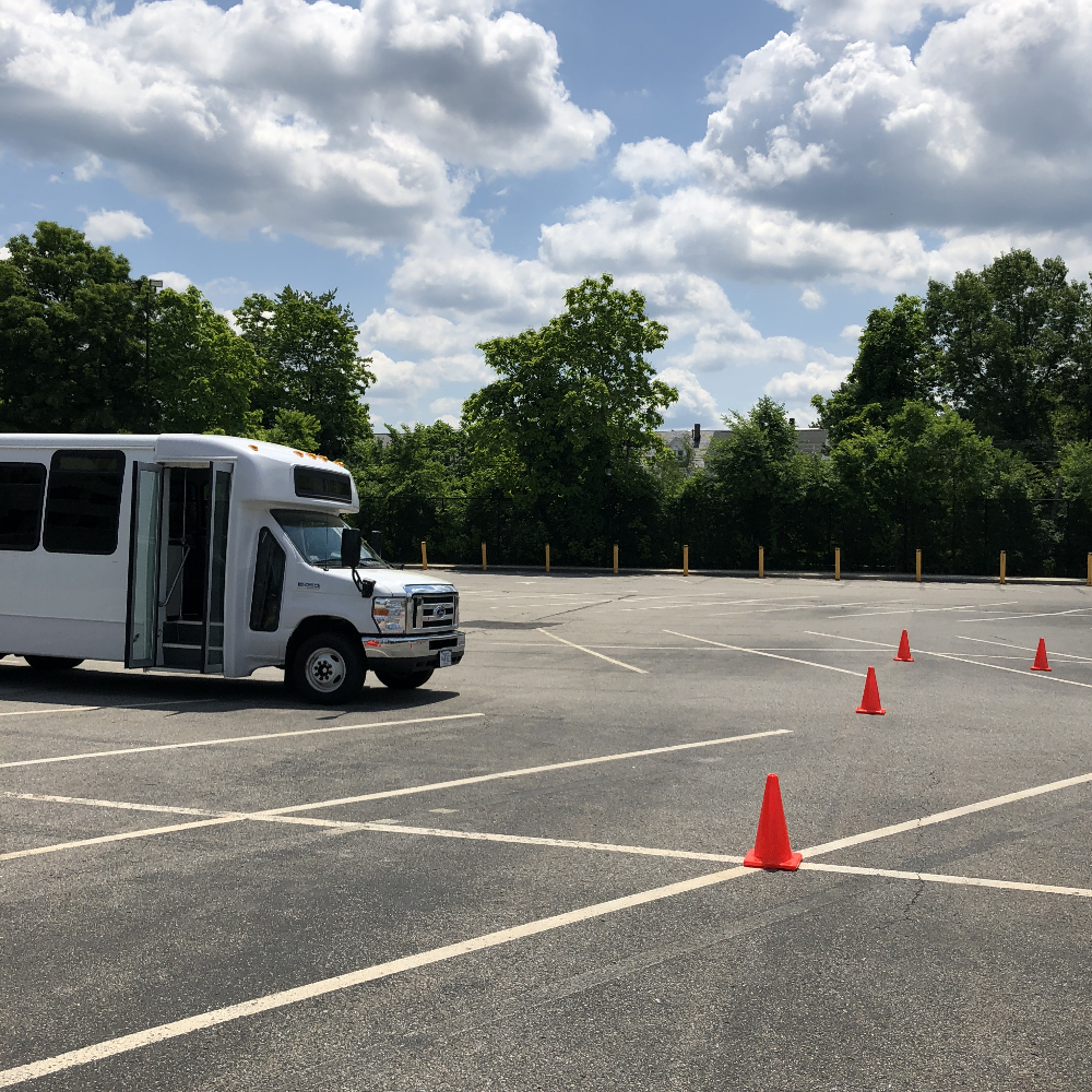 A shuttle bus in a parking lot surrounded by traffic cones. 