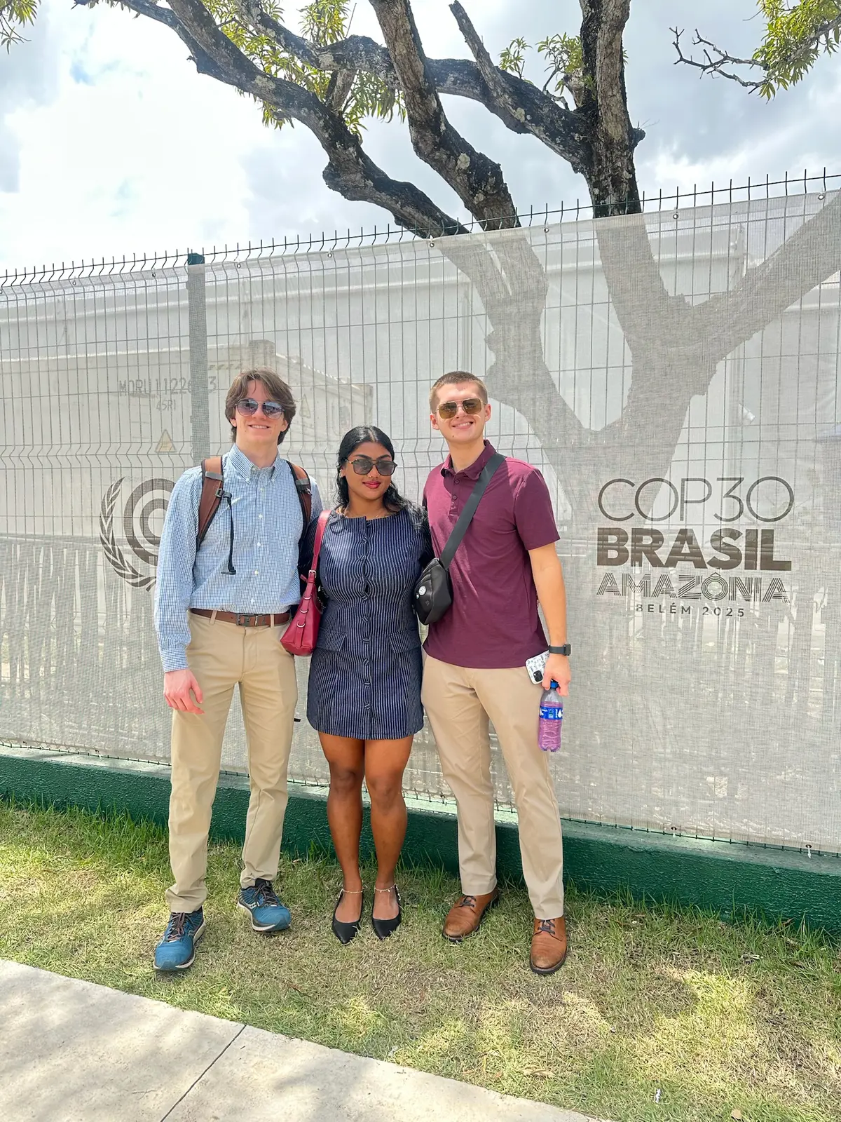 Three students pose in front of COP30 Brasil Amazonia sign.