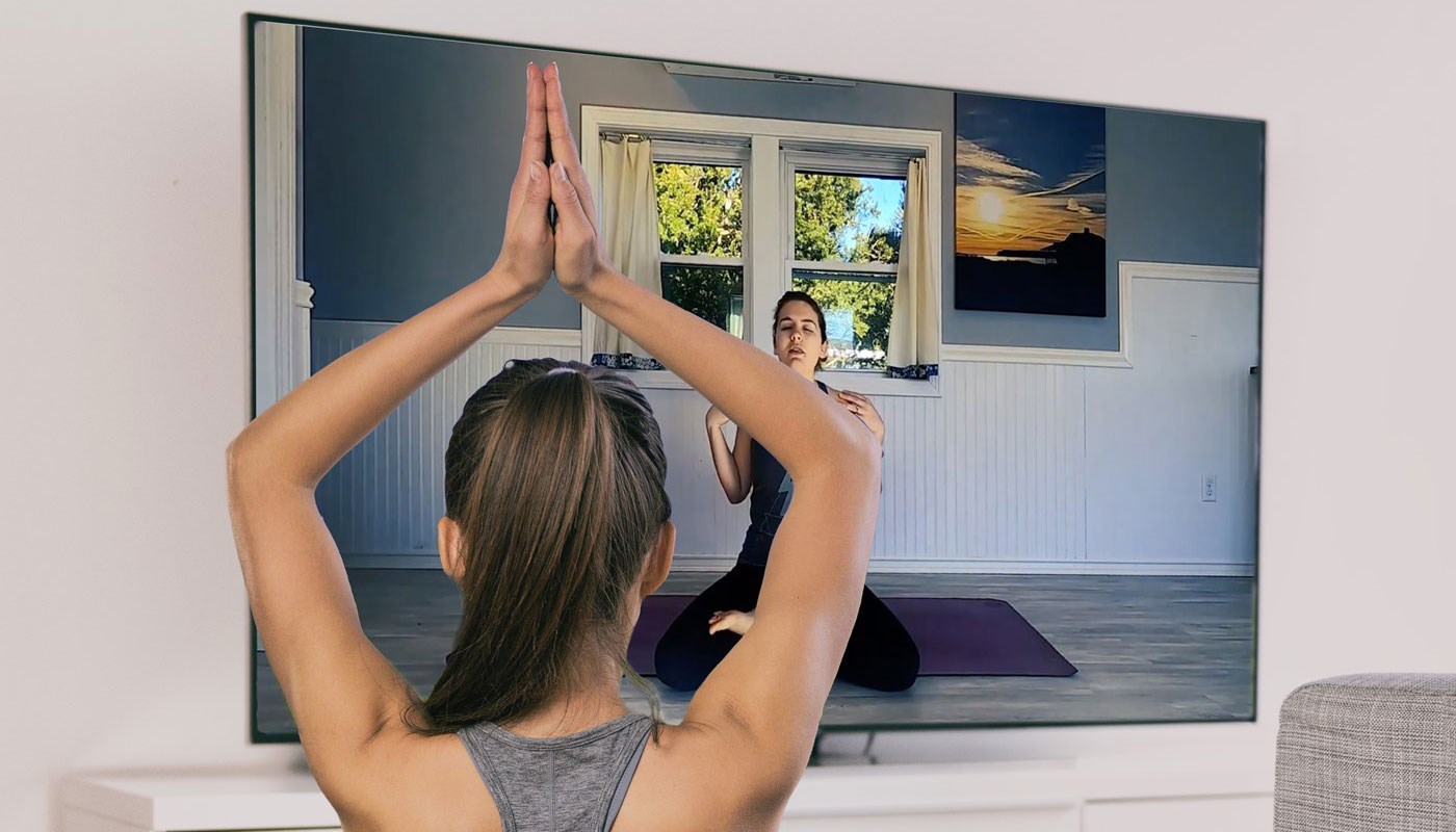 Young woman in foreground watches woman on screen teach yoga