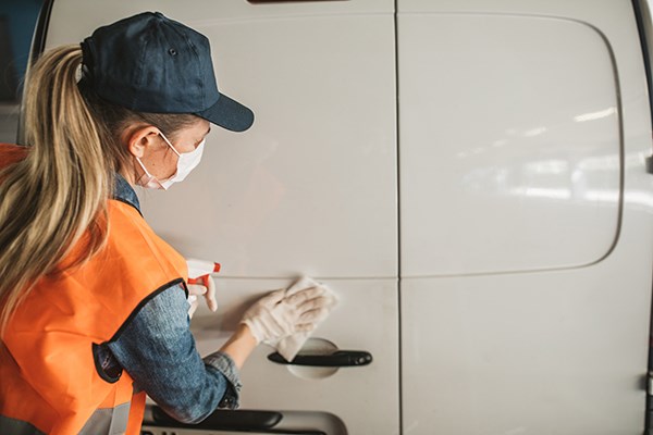 A worker wearing PPE cleans a food delivery van.