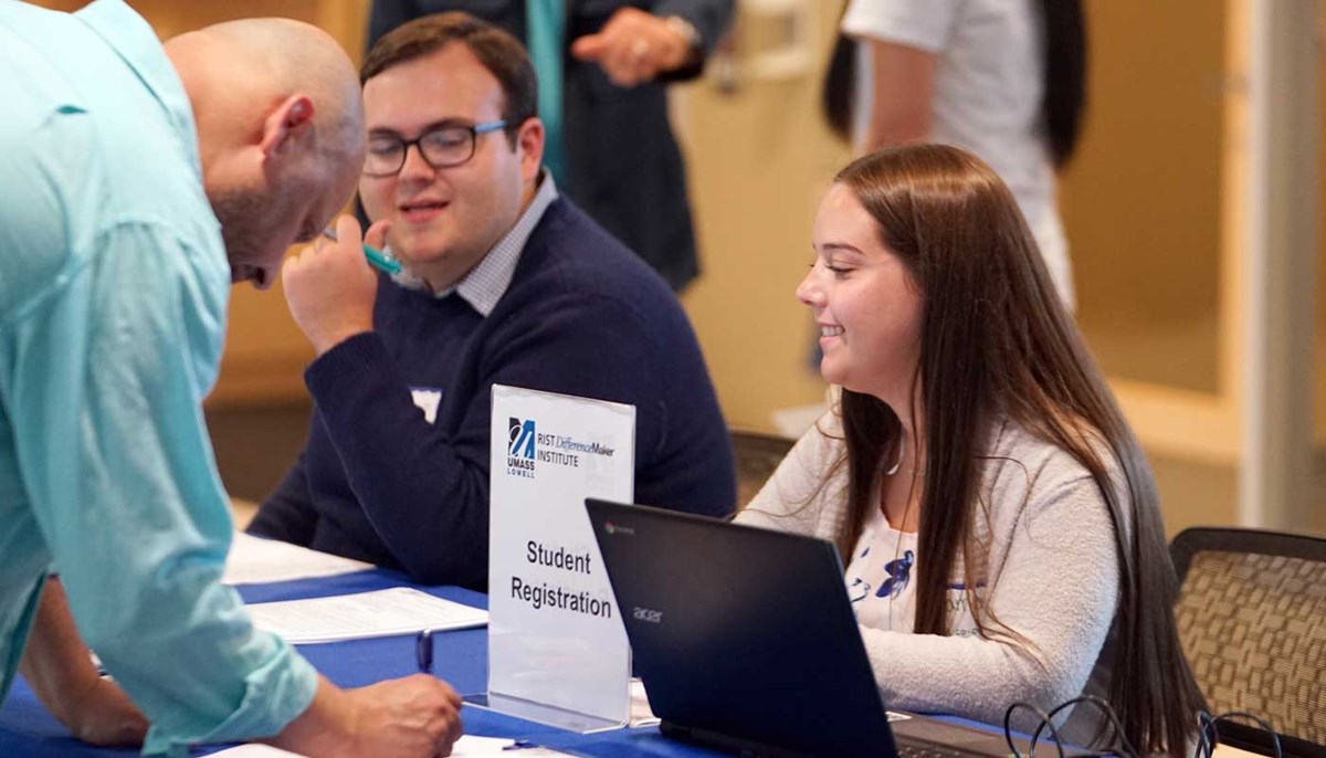 Cameron Famiglietti sits at a table to register students for a UMass Lowell DifferenceMaker event.