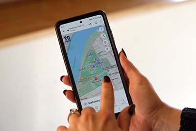 A person holds a smartphone and swipes on an image of a map on the screen