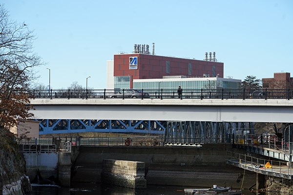 A student and a car cross a canal bridge with UML buildings in the background