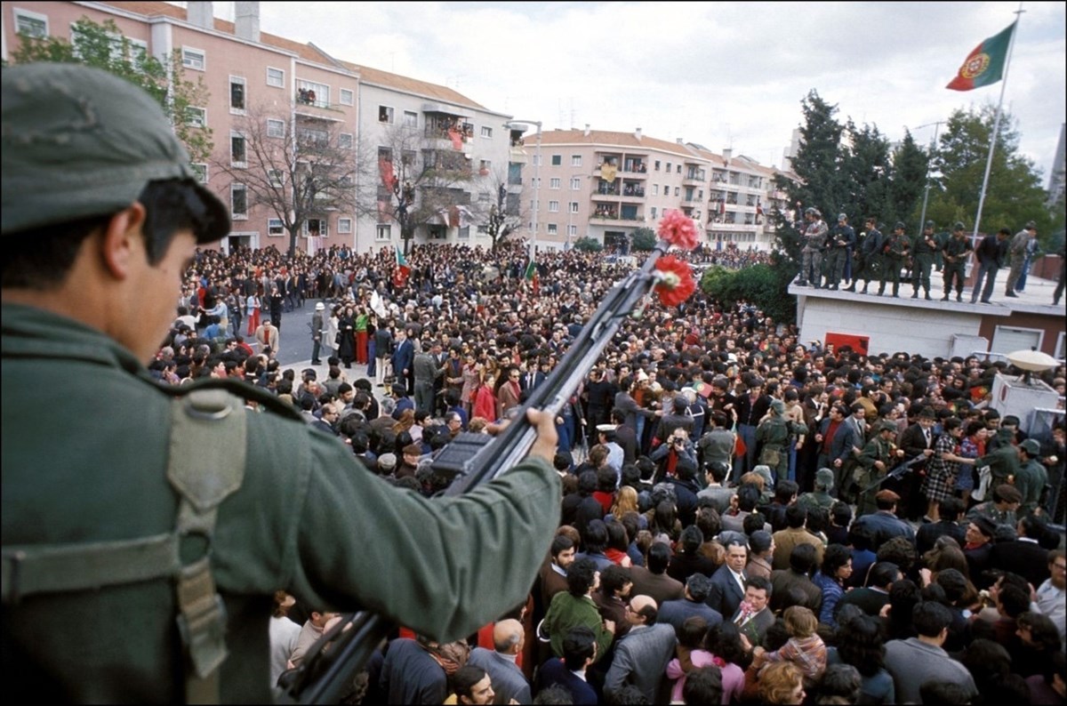 Carnation Revolution - a soldier in green holding a rifle with a sea of people below. 