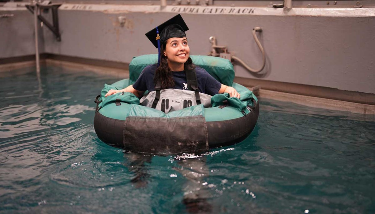 Cassia Fontes wears a graduation cap while she floats in an inflatable tube in a water tank at UMass Lowell
