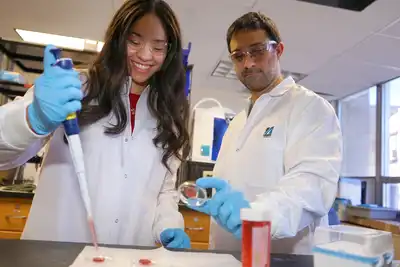 A young woman rolls up her sleeve while a woman scans her arm with a device attached to a mobile phone.