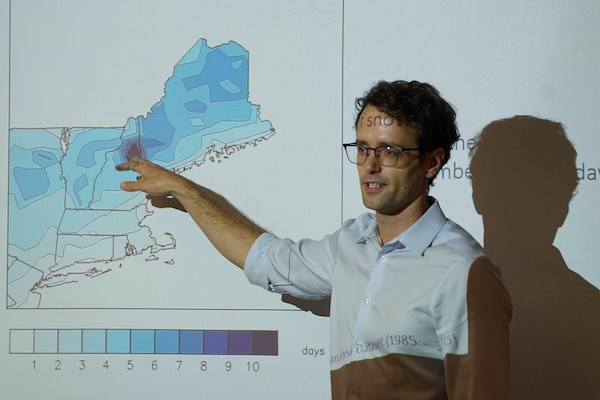 A man in glasses points to a map of New England projected on a screen