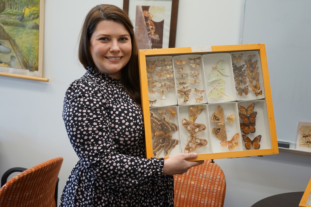 Christina Kwapich smiling and holding up a framed display of taxidermized butterflies.