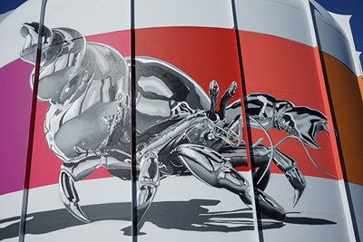 "Chrome Cobito" is a mural of a Caribbean hermit crab against a band of colors on a round building at UMass Lowell