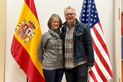 A man and a woman pose for a photo in front of flags of Spain and the United States