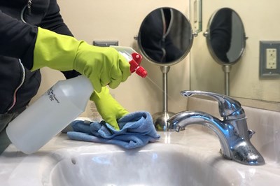 Person with green gloves spraying a cleaning solution on a bathroom handle