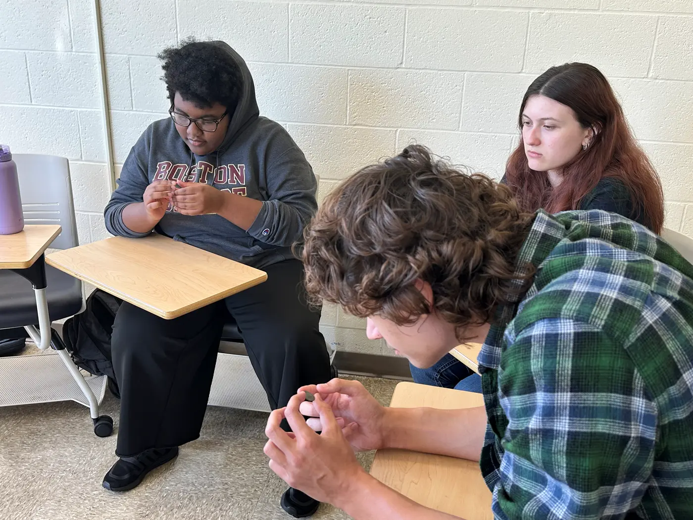 Three students, including history major Brandon Bulman, peer at ancient coins in a classroom