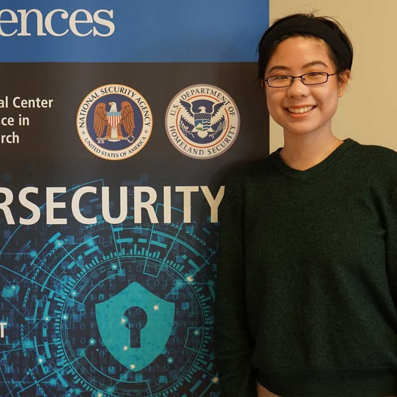 Student posing next to a sign for a cybersecurity conference at UMass Lowell
