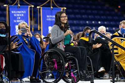 Alumna Sanskriti Sharma, who is in a wheelchair, holds a microphone and talks to students
