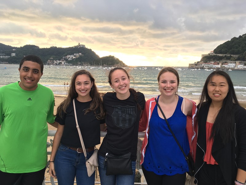 Corrina Quaglietta abd four other study abroad students pose for a photo in front of the sun setting on a beach in San Sebastian, Spain