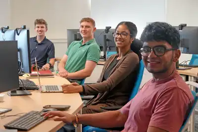 Four students sit in front of computers.